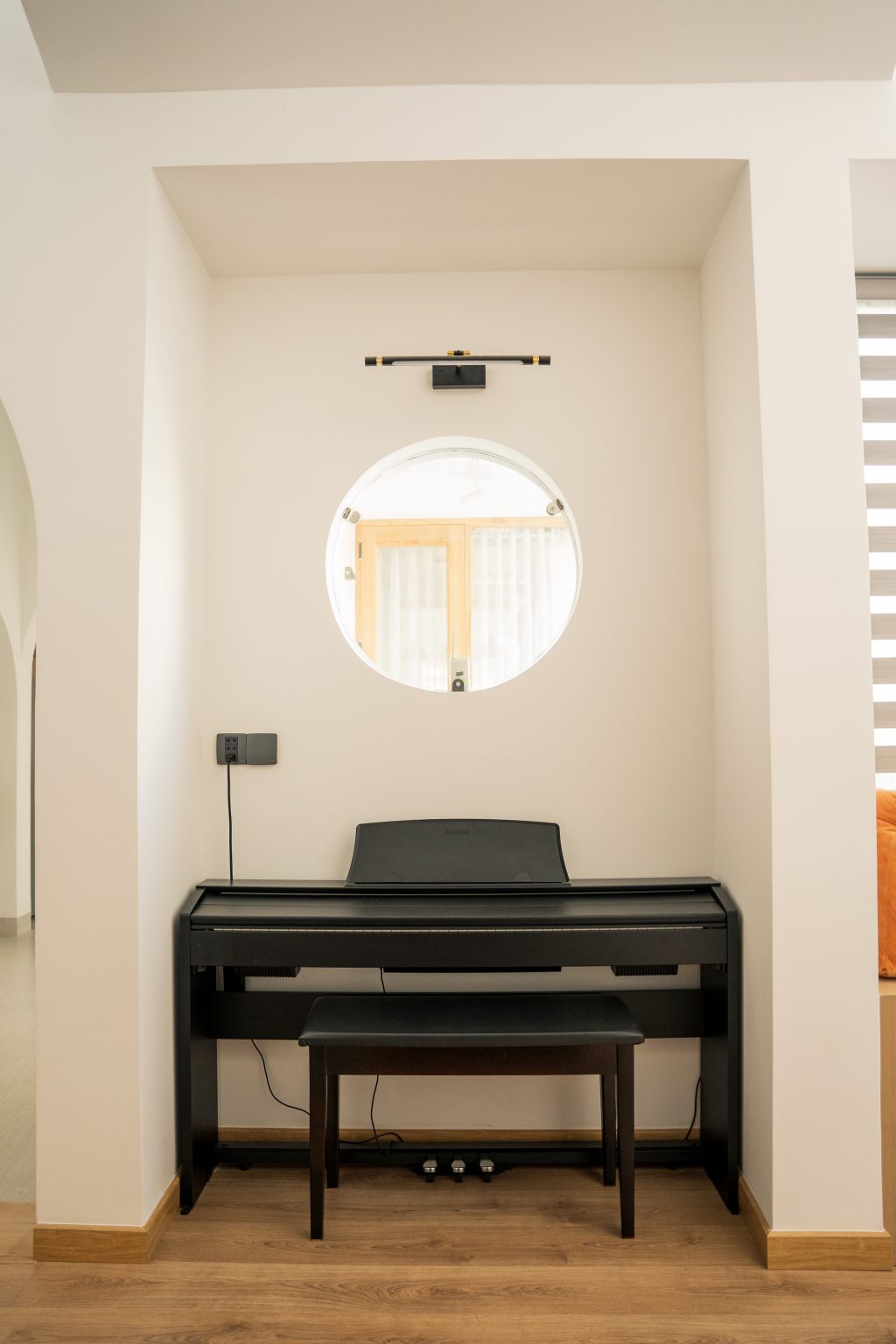 Góc đặt đàn piano dưới ô cửa sổ tròn trong hốc tường trắng