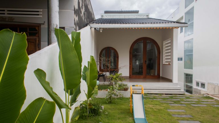 Hiên nhà rộng với cửa vòm gỗ và cầu trượt nhỏ cho bé trên sân cỏ