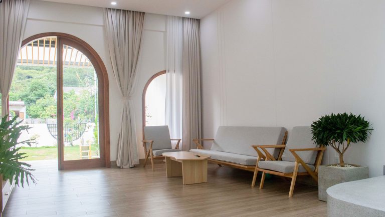 Góc phòng khách với cửa vòm kính, sofa gỗ và sàn gỗ màu sáng